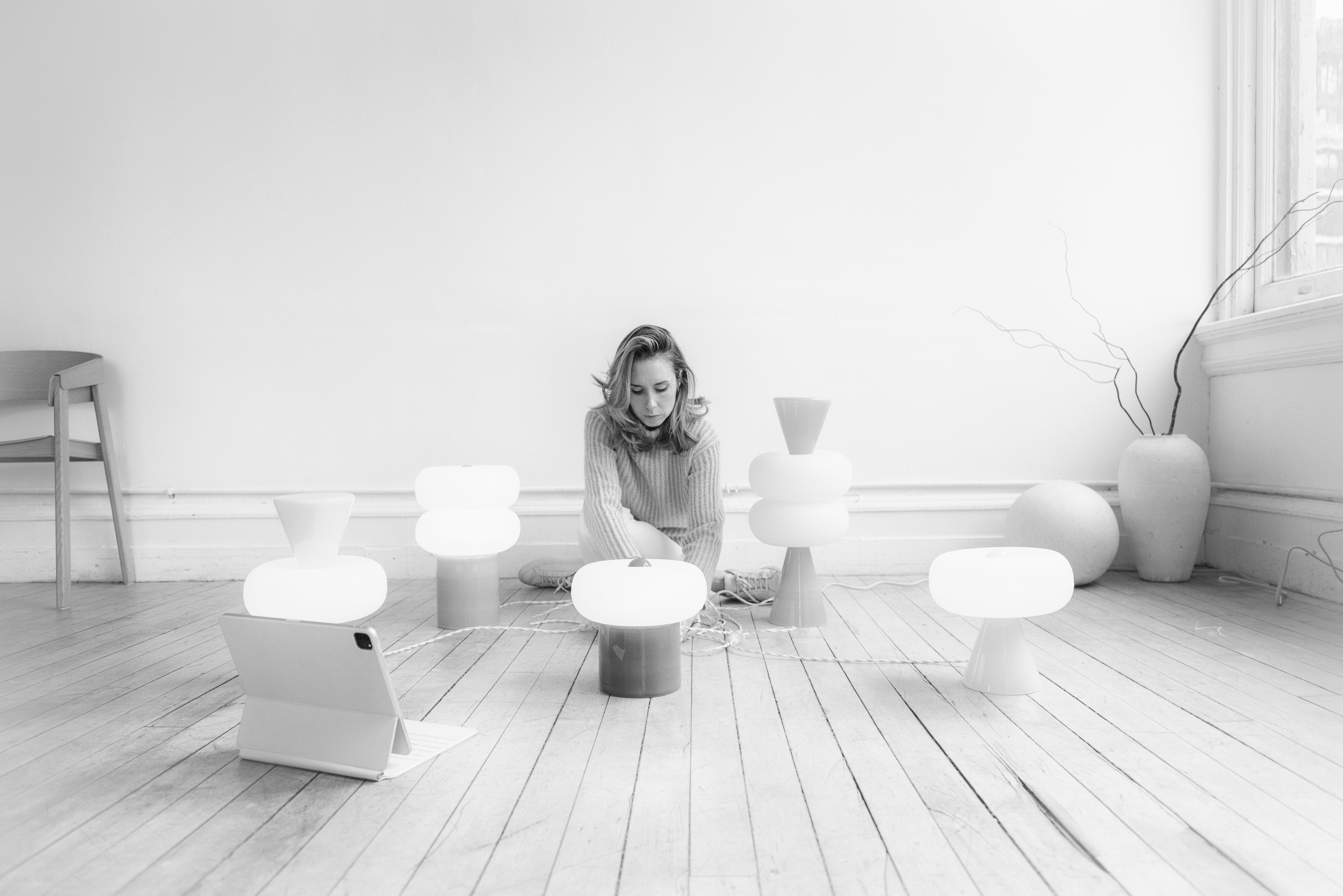 Black-and-white portrait of the designer seated among several of Noiro Studio's table lamps and an iPad